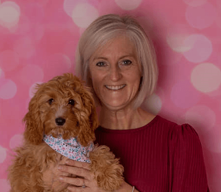 A woman standing behind a pink background holding a puppy