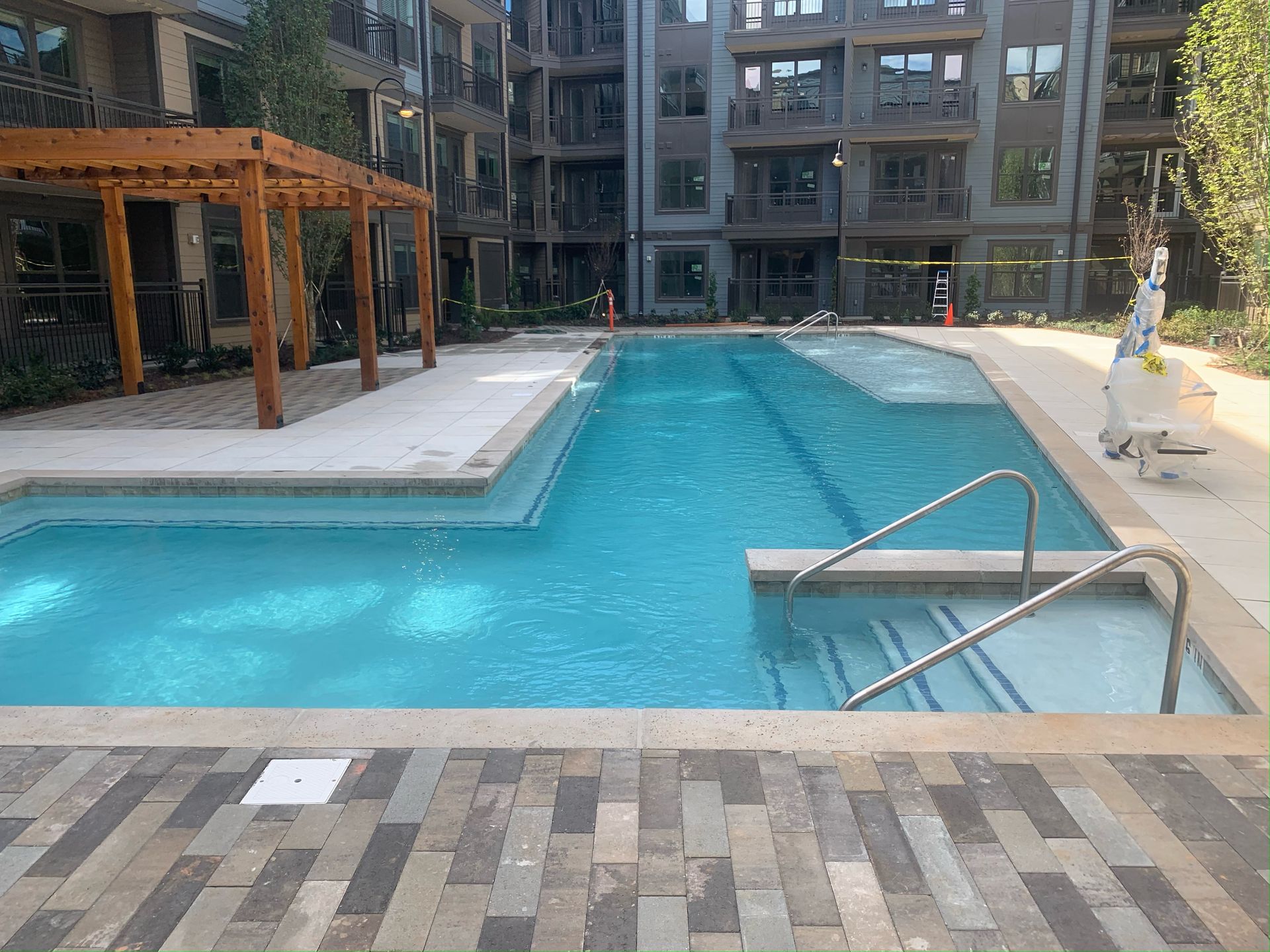 A rectangular swimming pool with a shallow lounge area and steps, set in a courtyard between modern apartment buildings.