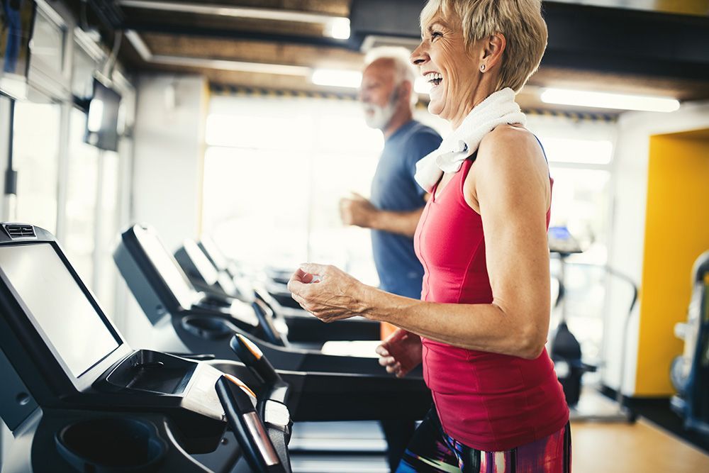 An elderly couple is running on treadmills in a gym.