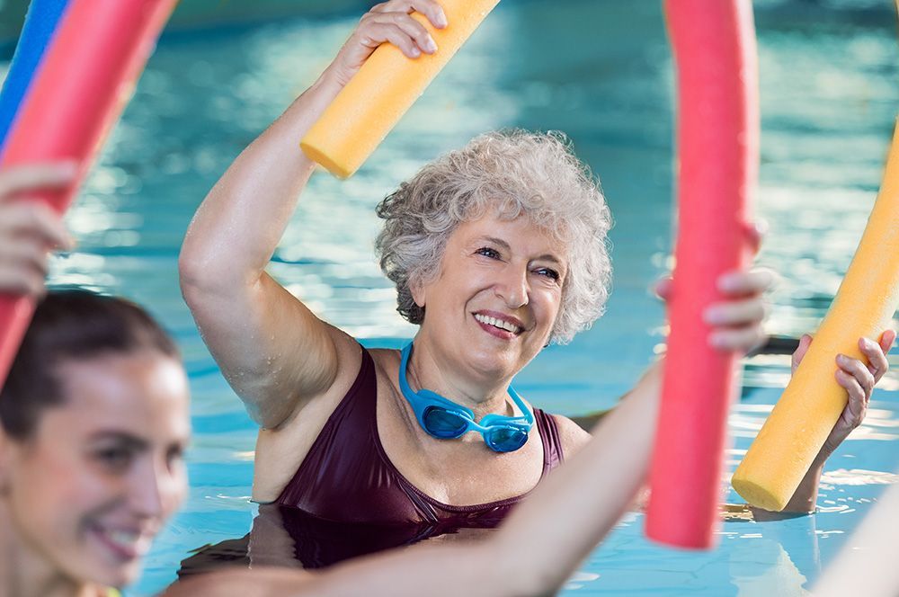 A group of women are holding foam noodles in a swimming pool.