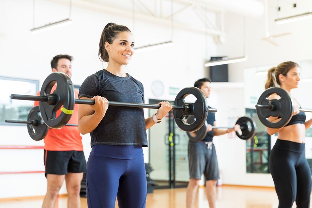 A group of people are lifting barbells in a gym.