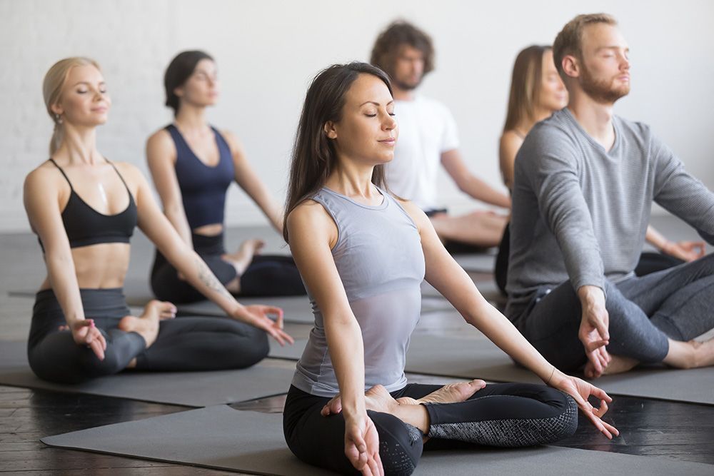 A group of people are sitting on yoga mats with their eyes closed.