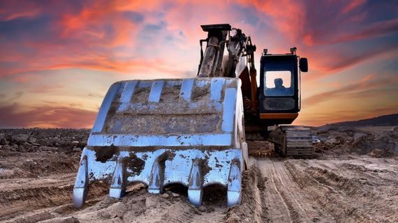 A bulldozer is moving dirt in a dirt field at sunset.