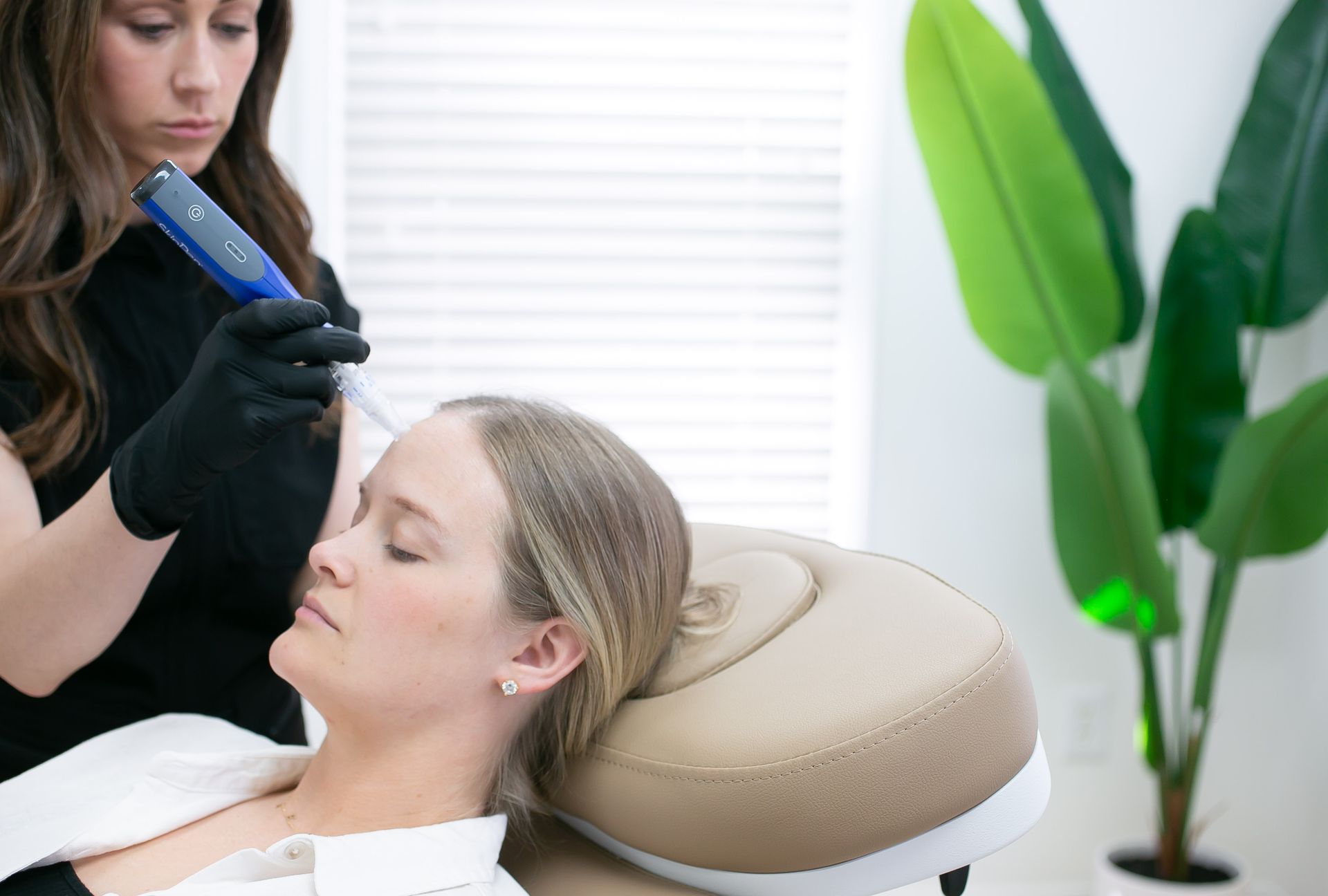 Woman receiving scalp treatment at a clinic. Practitioner with black gloves uses a device on the woman's scalp.