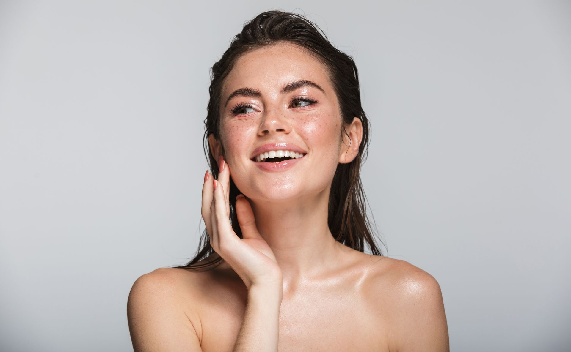 Woman with wet hair smiling, touching her cheek, glowing skin, and looking up.