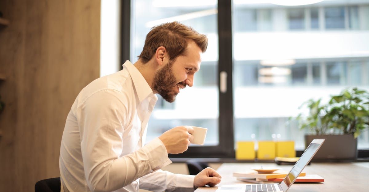 A man is drinking coffee while using a laptop computer.