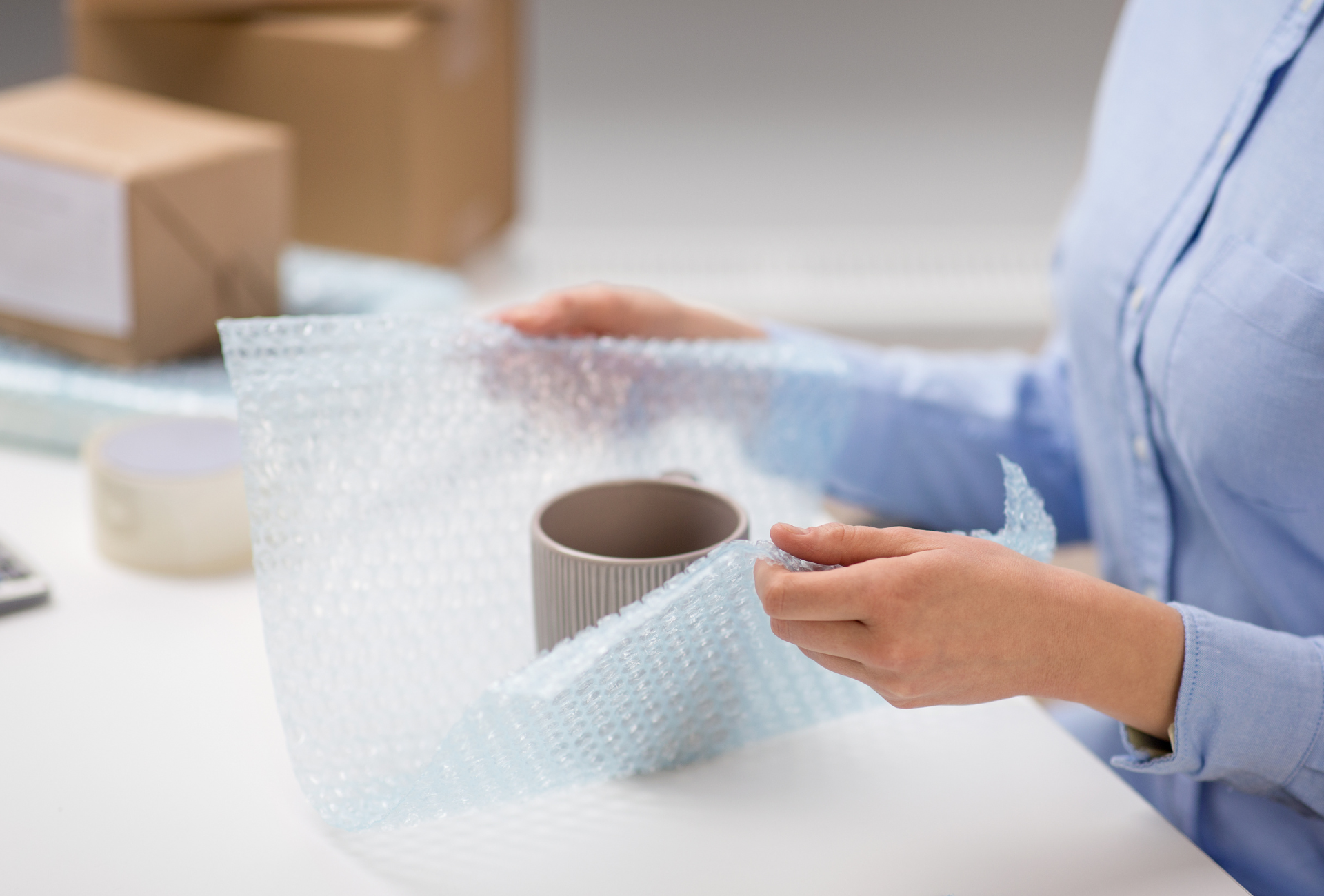 A woman is wrapping a cup with bubble wrap.
