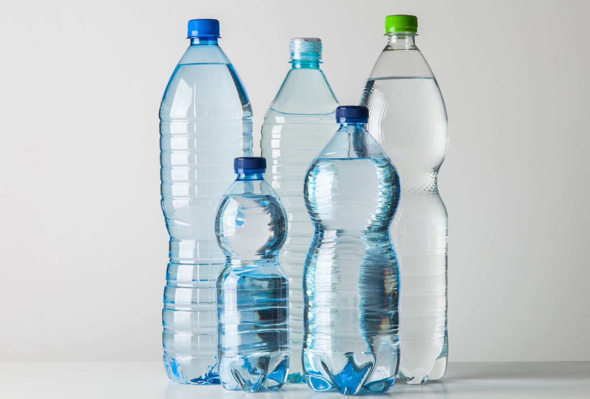 A group of plastic water bottles of different sizes are lined up on a table.