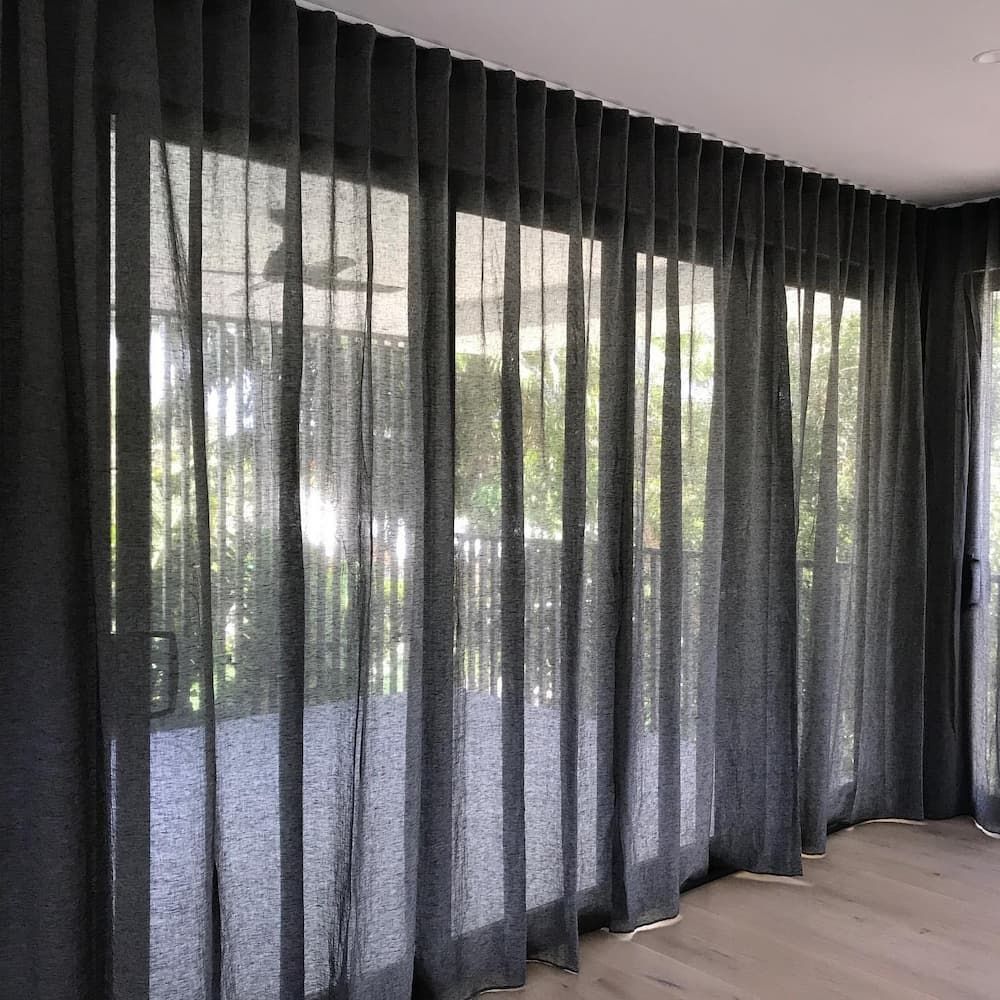 Sheer Black Curtains Hang From Ceiling to Floor in Front of Large Windows