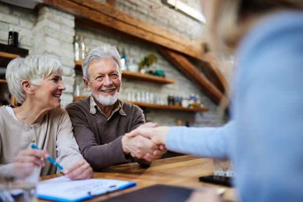An elderly couple is shaking hands with a woman while sitting at a table.