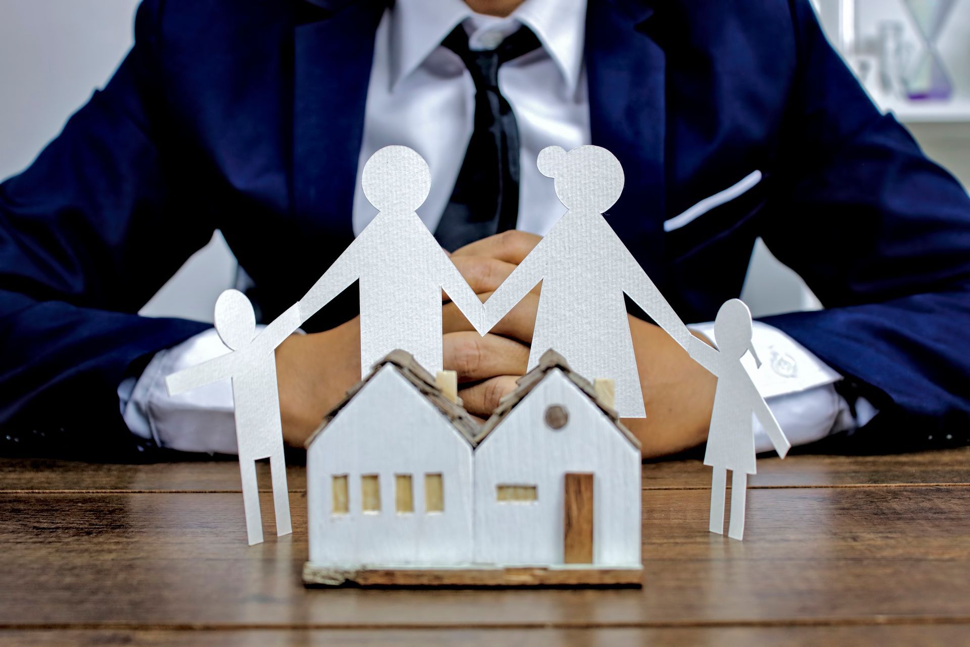 A man in a suit and tie is sitting at a table with a paper cut out of a family and a house.