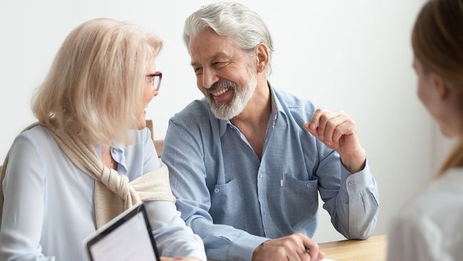 An elderly couple is sitting at a table talking to a health insurance broker.