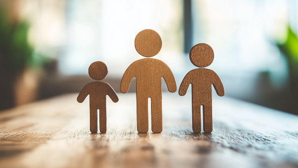 Three wooden figures of a family standing next to each other on a wooden table.