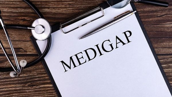 A clipboard with the word medigap written on it and a stethoscope on a wooden table.