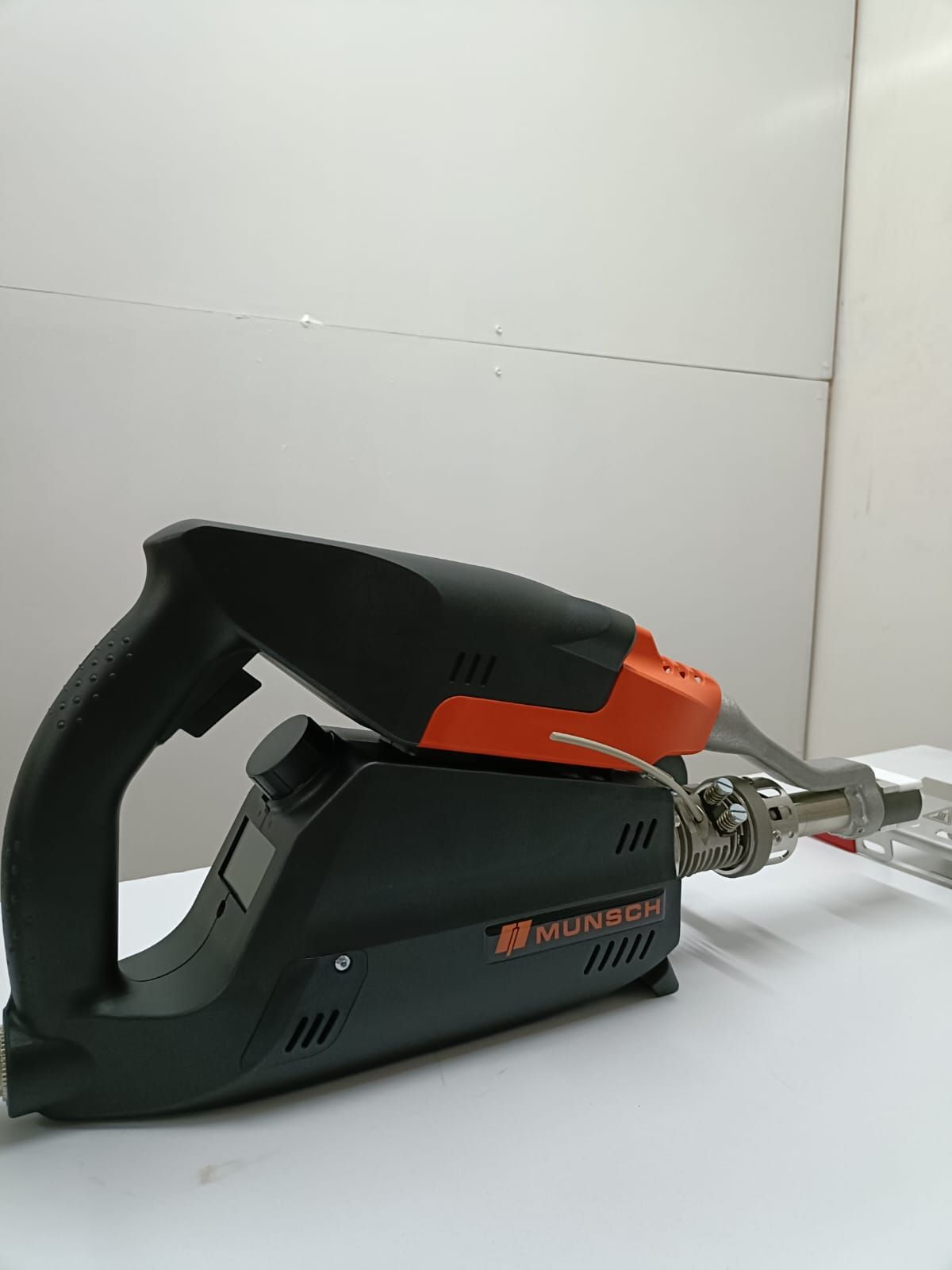 Pistola de soldar Munsch negra y naranja sobre una superficie blanca.