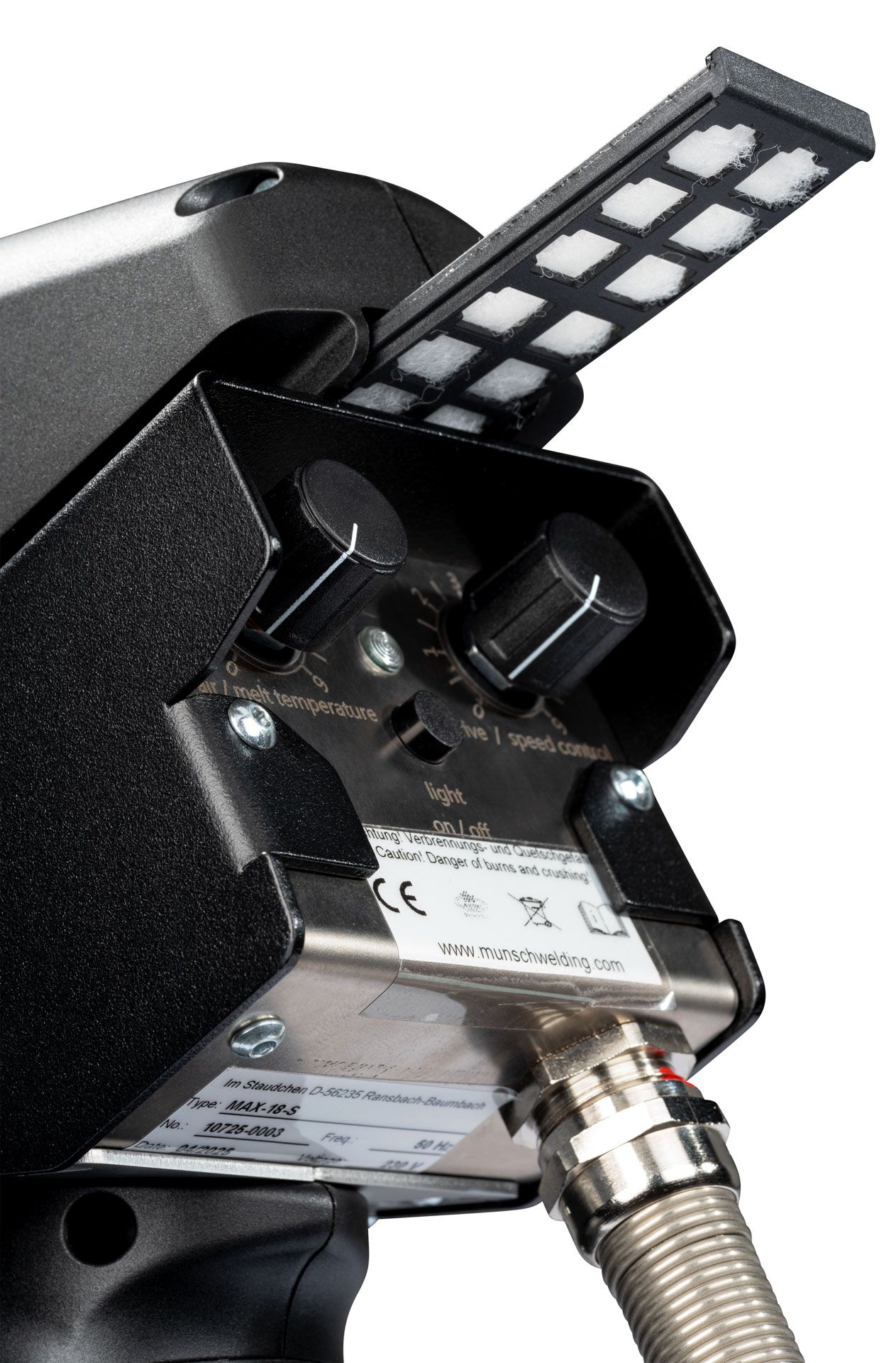 Primer plano de una máquina industrial negra con un dial de control de temperatura, un cartucho de cuadrados pequeños y una manguera enrollada.