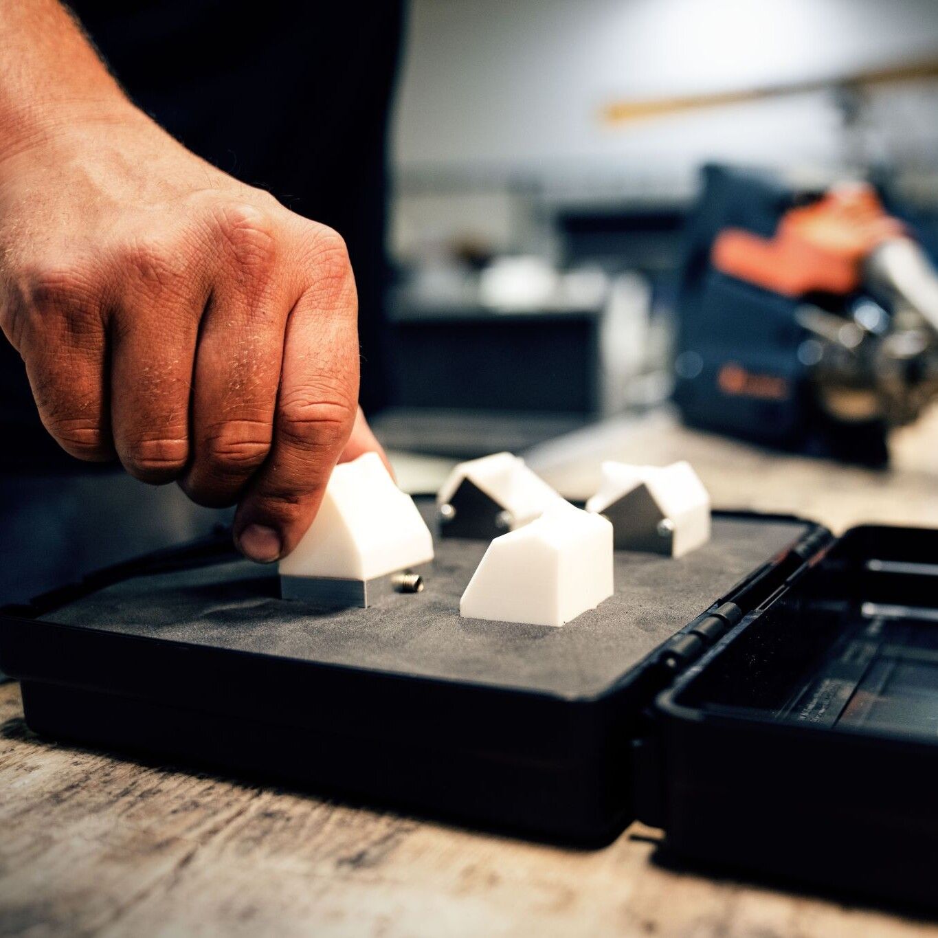 Una mano colocando un objeto blanco y angular dentro de un estuche negro con otros objetos similares.