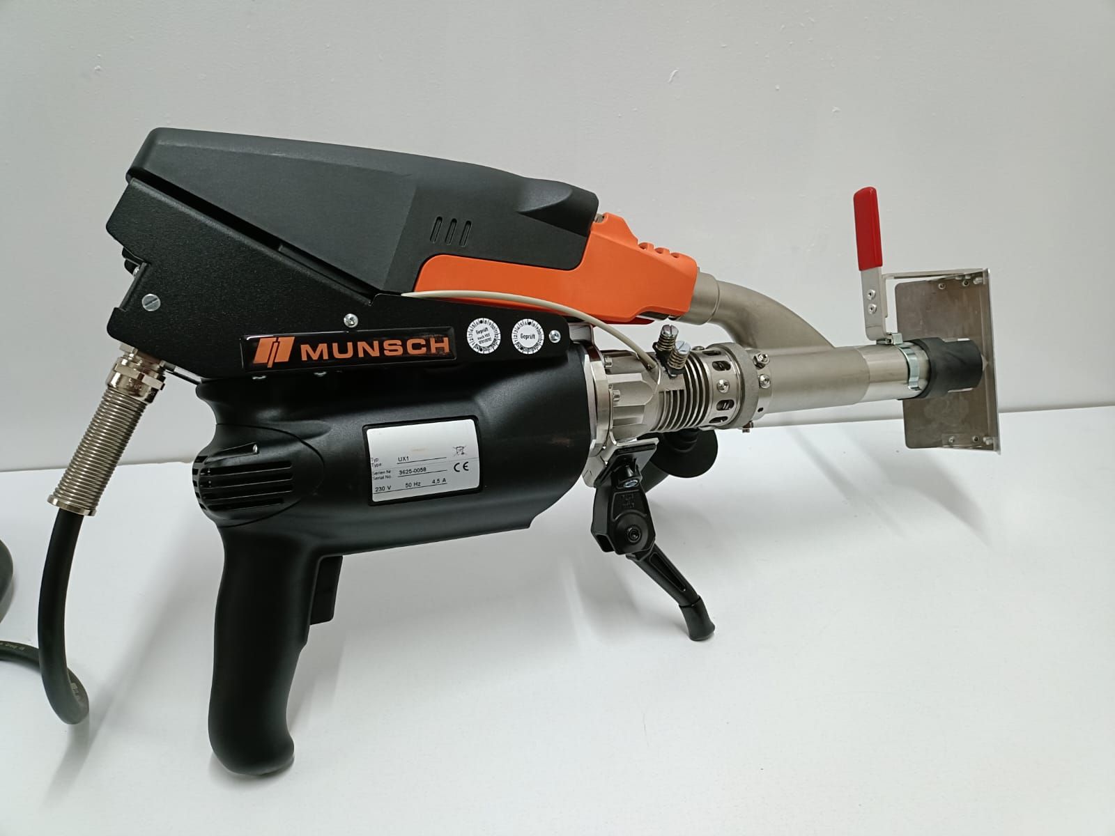 Soldador de aire caliente Munsch negro y naranja sobre una superficie blanca con una boquilla plateada.