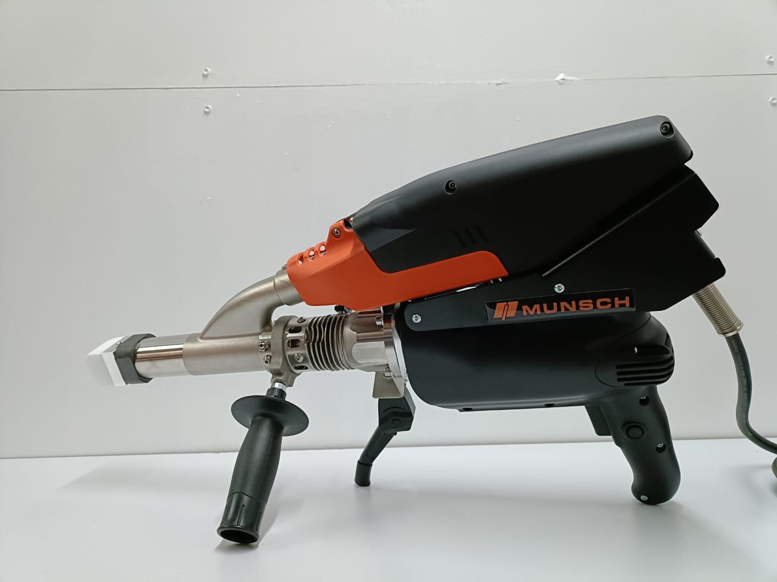 Herramienta de soldadura de color naranja y negro sobre una superficie blanca con fondo gris.