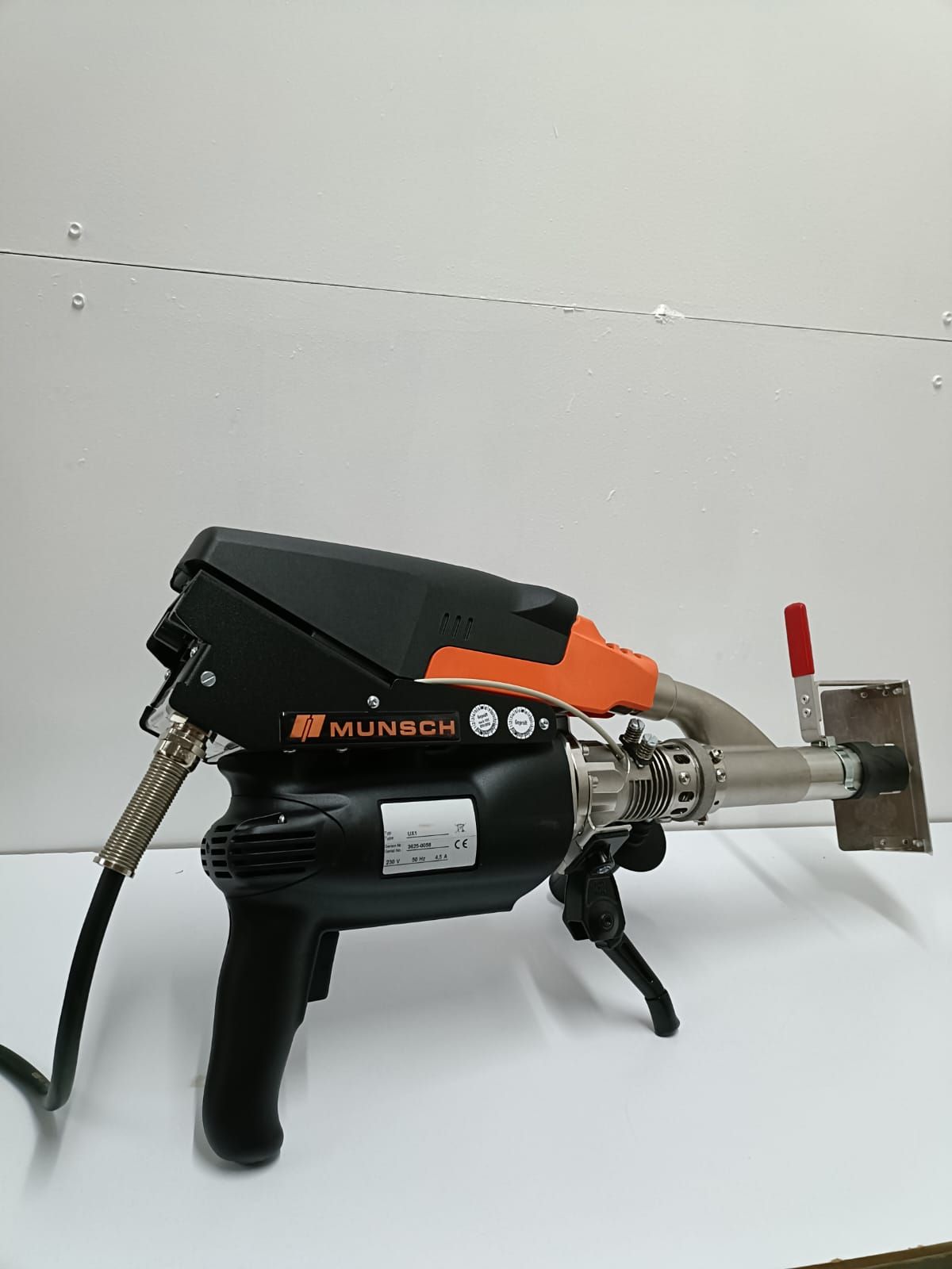 Herramienta de soldadura Mundor negra y naranja sobre una superficie blanca, con una boquilla plateada y una manguera negra.