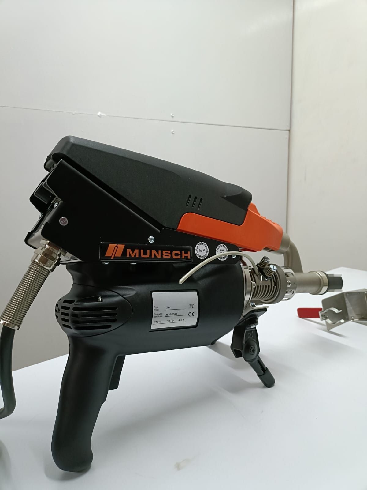 Herramienta de soldadura Munch de color negro y naranja sobre una superficie blanca, con manguera flexible y mango.