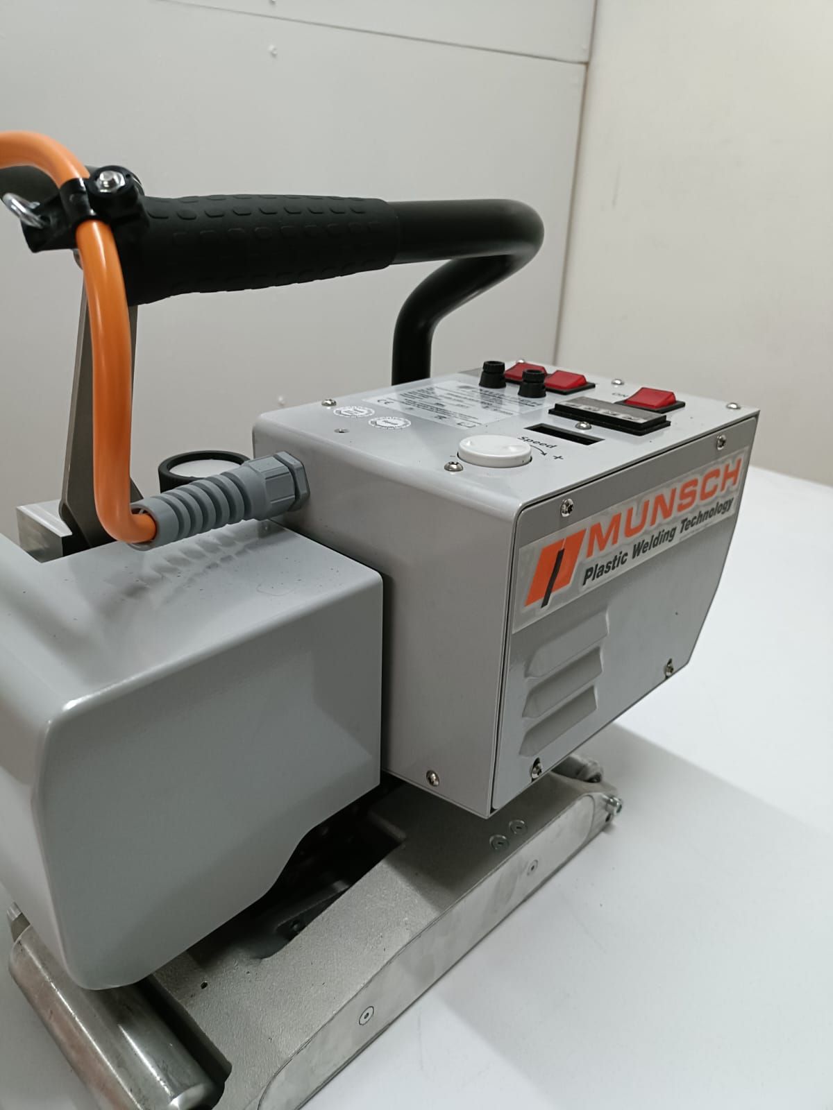 Máquina de soldar de plástico Munsch de color gris y naranja sobre una superficie blanca con mango negro.