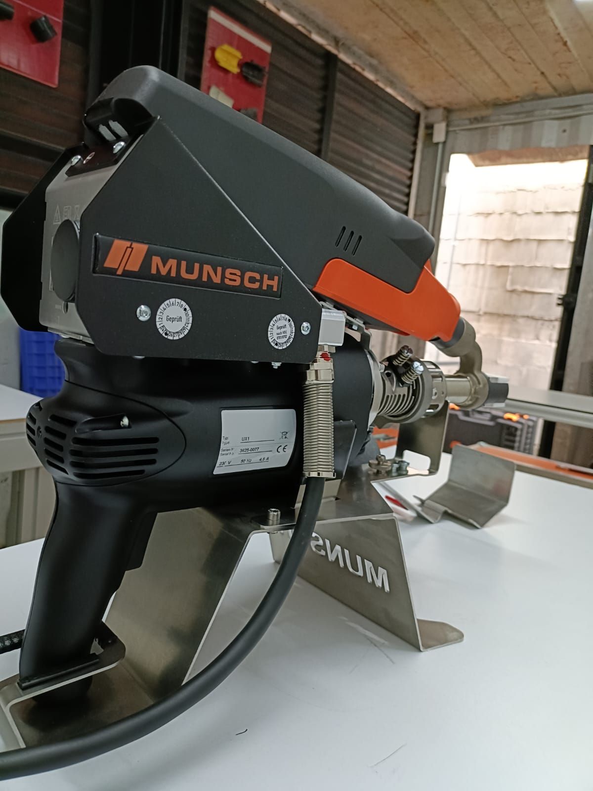 Herramienta de soldadura Munsch sobre soporte de metal, esquema de color negro y naranja, en interiores sobre una superficie blanca.