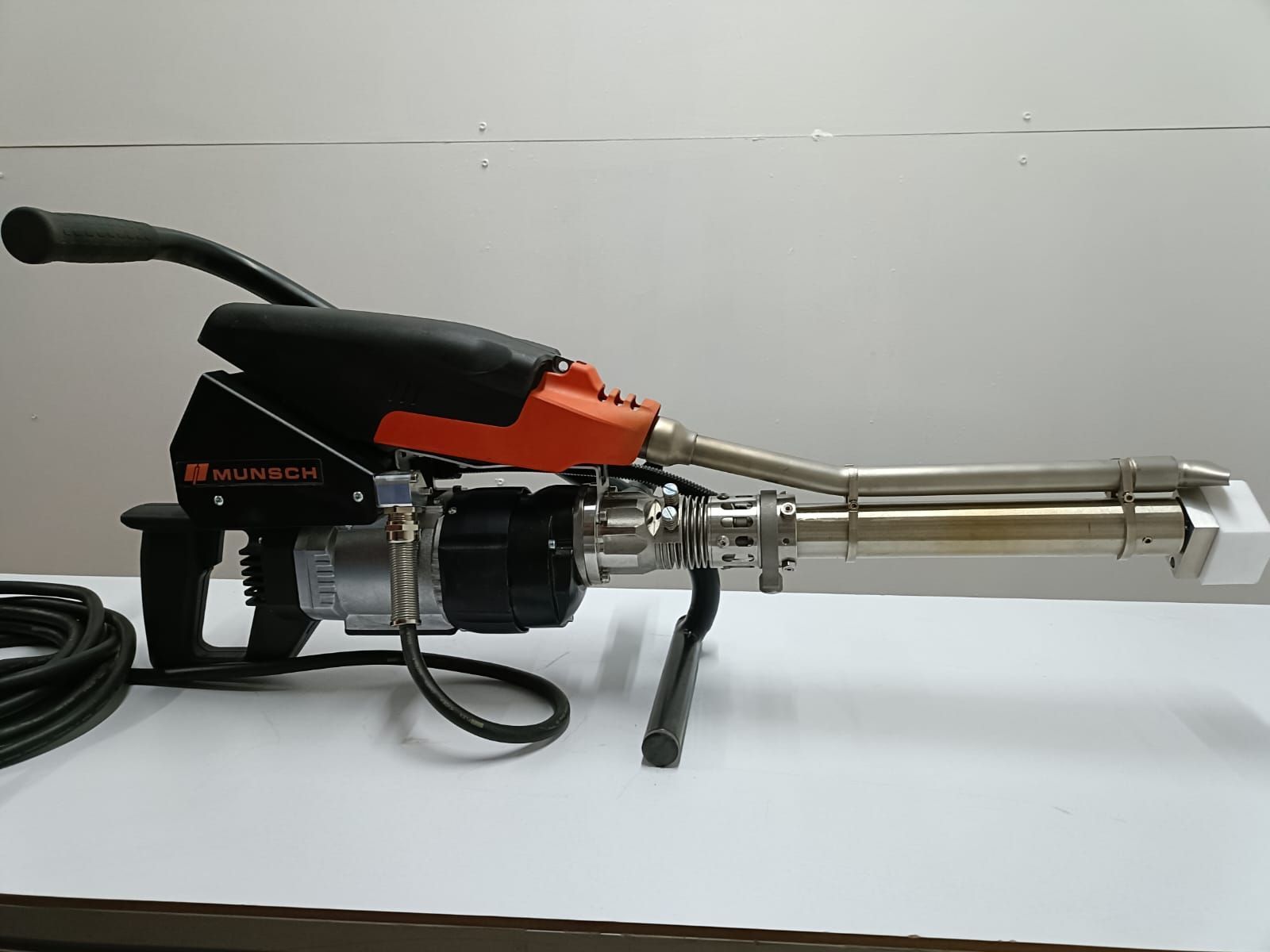 Herramienta de soldadura manual de plástico, de color negro y naranja, sobre superficie blanca, con cabezal de soldadura de metal.