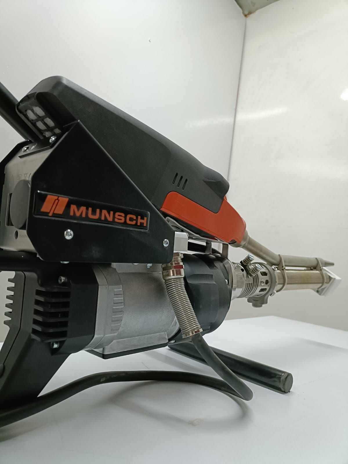 Herramienta de soldadura Munsch de plástico negro y plateado con detalles en naranja, sobre un soporte.