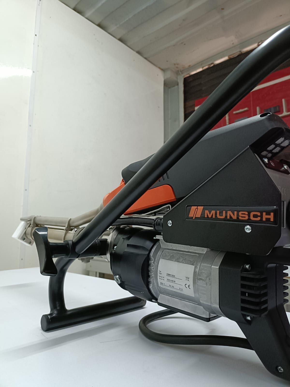 Herramienta de soldadura de tuberías Munsch de color naranja y negro sobre una superficie blanca con un fondo blanco y rojo.