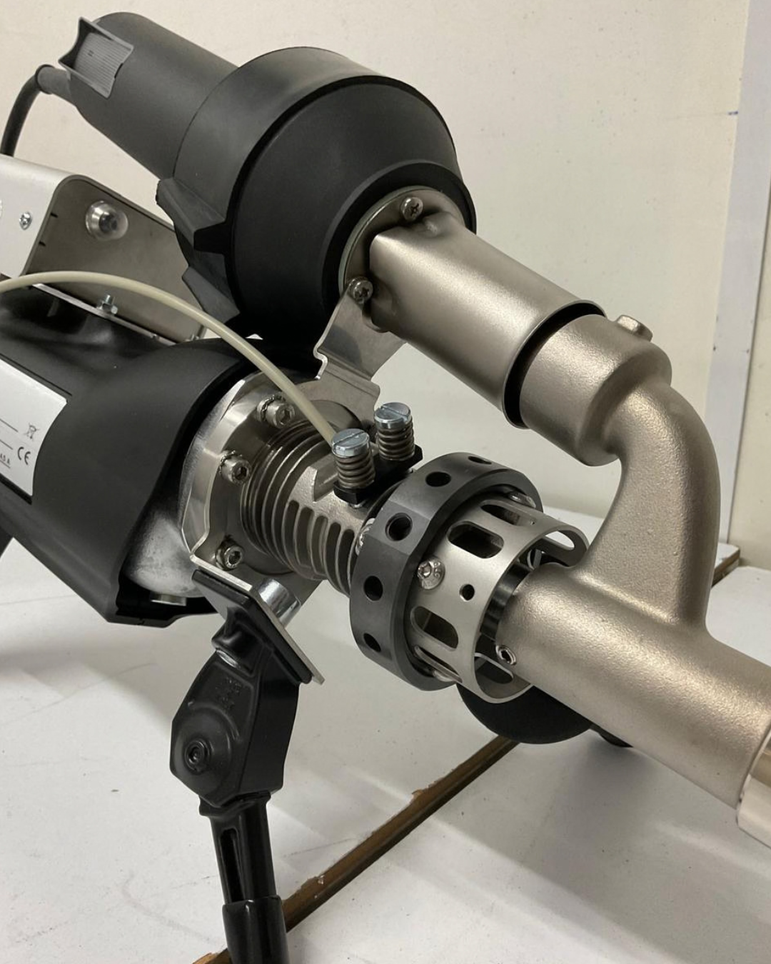 Herramienta de soldadura Mundor negra y naranja sobre una superficie blanca, con una boquilla plateada y una manguera negra.