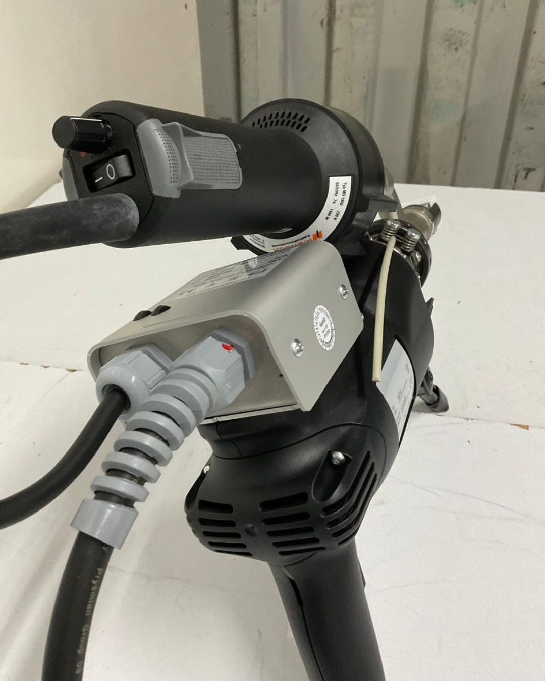 Soldador de aire caliente Munsch negro y naranja sobre una superficie blanca con una boquilla plateada.