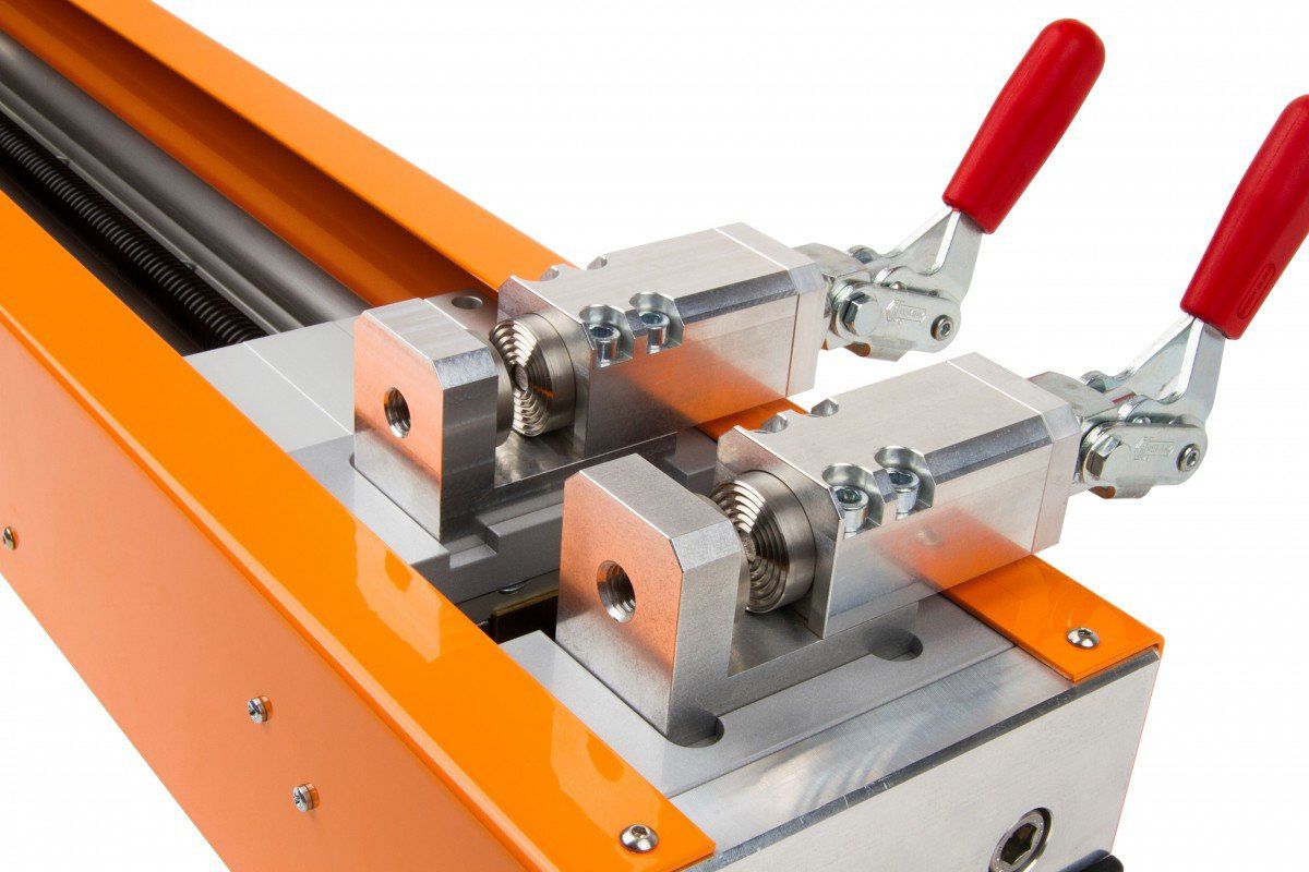 Máquina industrial de color naranja con dos abrazaderas plateadas, manijas rojas y rieles plateados.