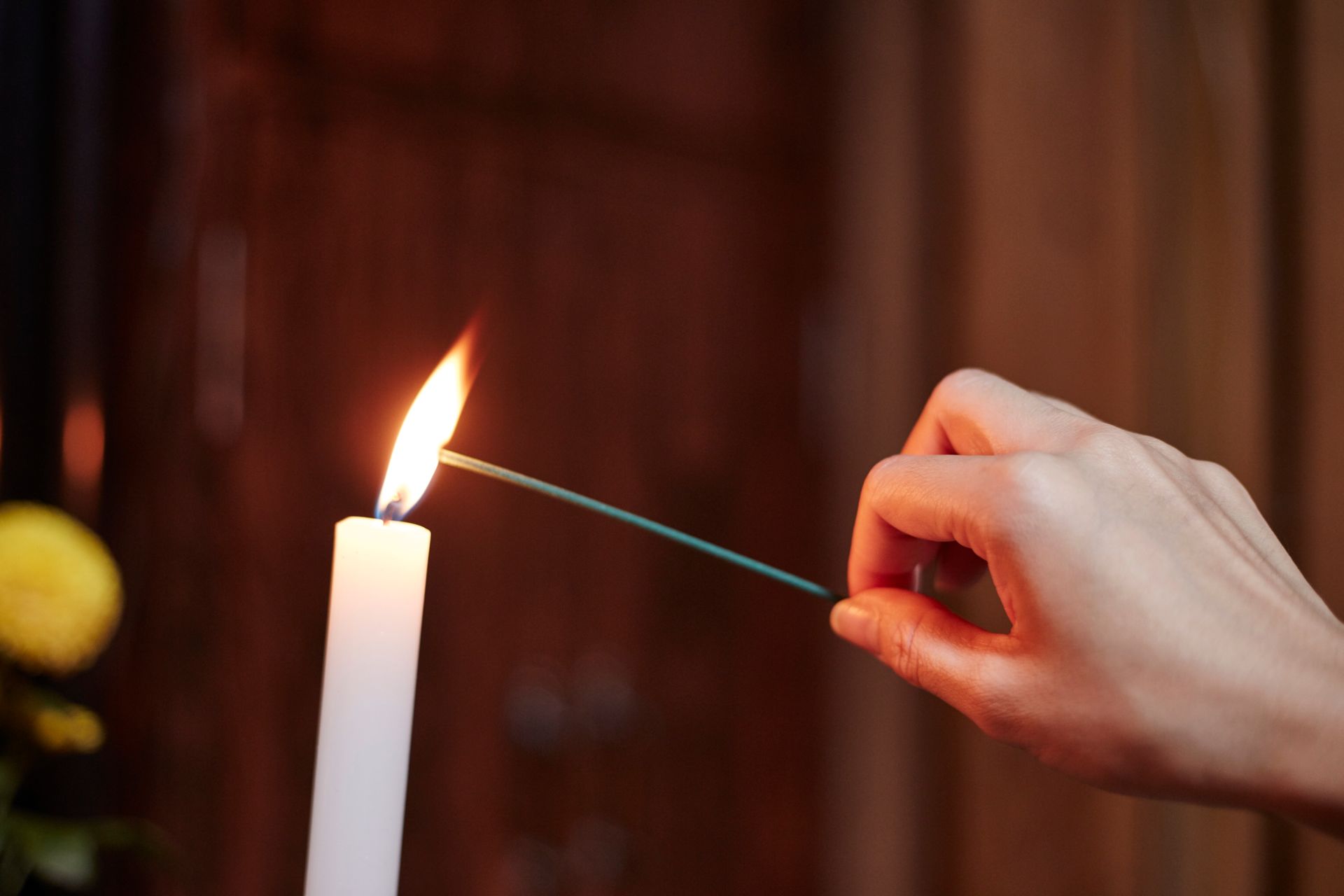 Accensione manuale di un bastoncino di incenso da una candela bianca accesa.