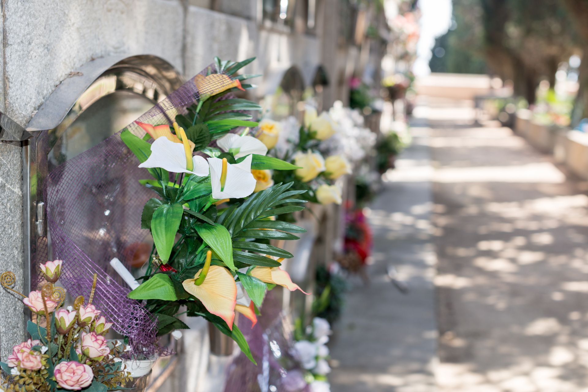Una persona in abito nero tiene in mano una rosa bianca durante una cerimonia funebre con candele e composizioni floreali.