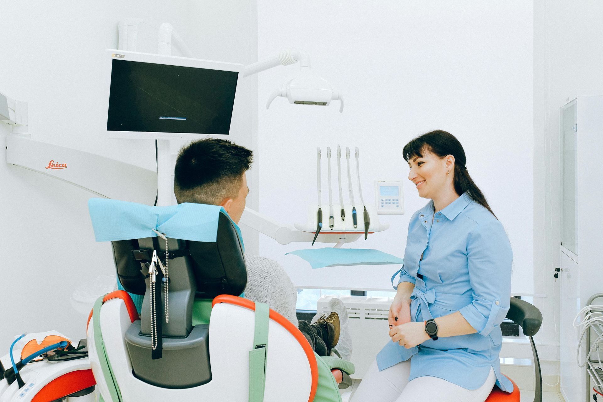 Dentist examining a smiling woman's teeth with dental tools in a bright office.