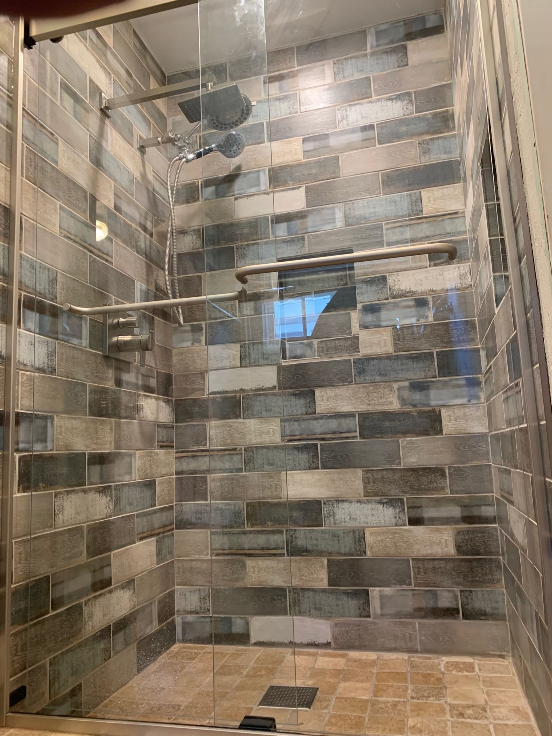 A shower with a brick wall and a glass door.