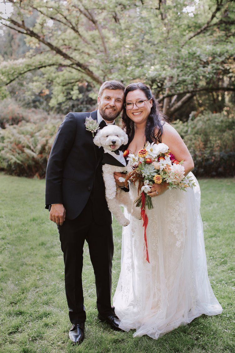 A bride and groom are posing for a picture with their dog.