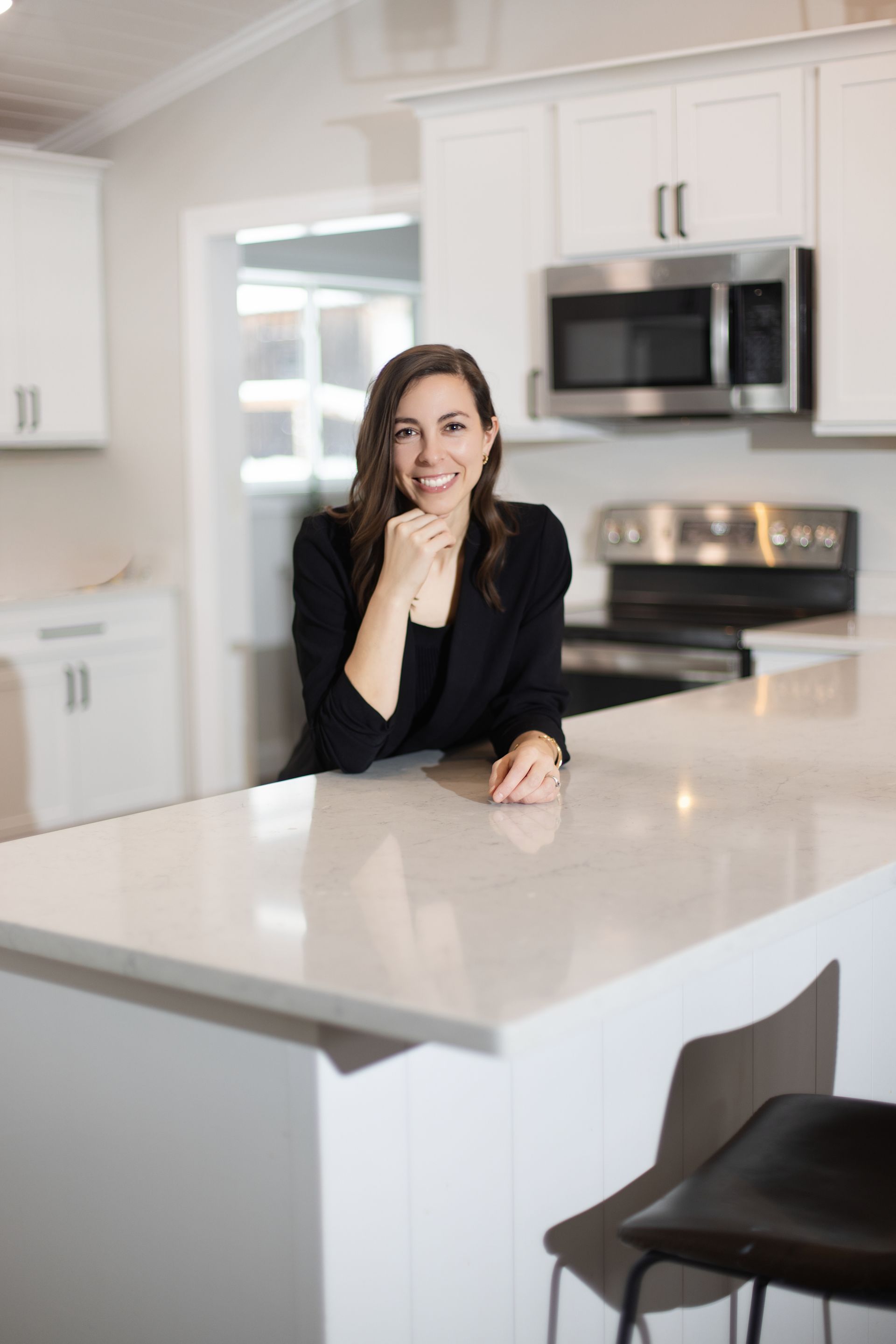Woman smiling while leaning on a white kitchen island in a bright, modern kitchen.