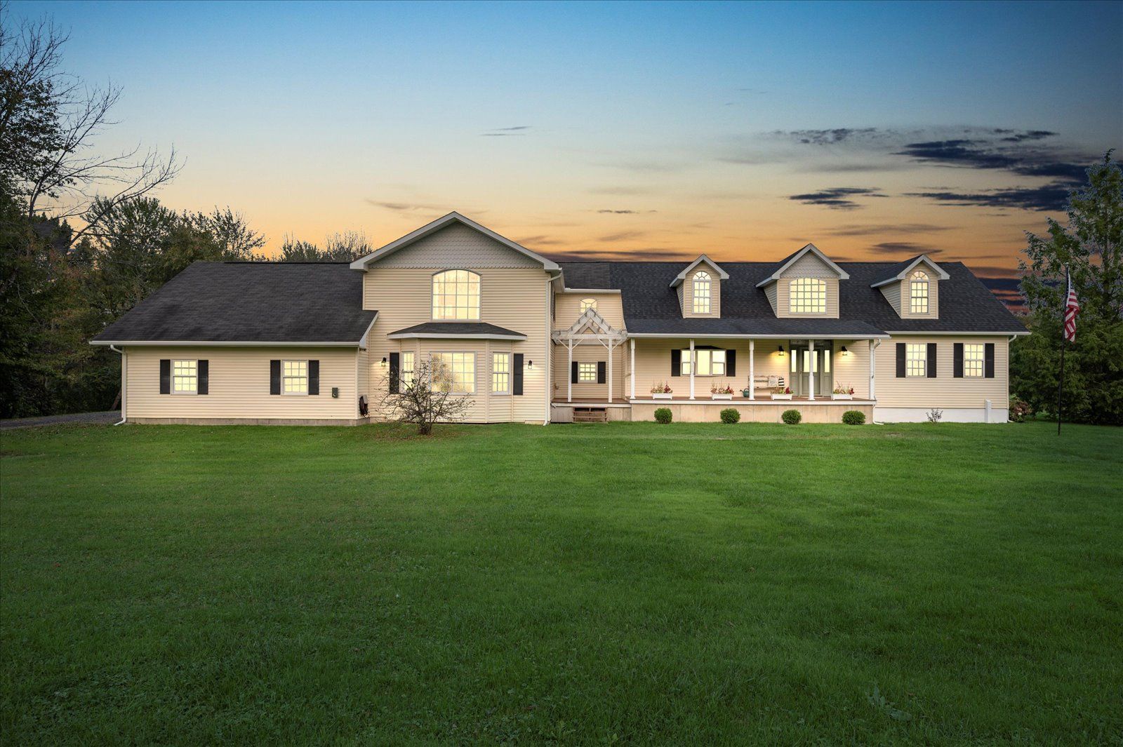 Large single-family home with a covered porch and expansive front lawn at sunset.