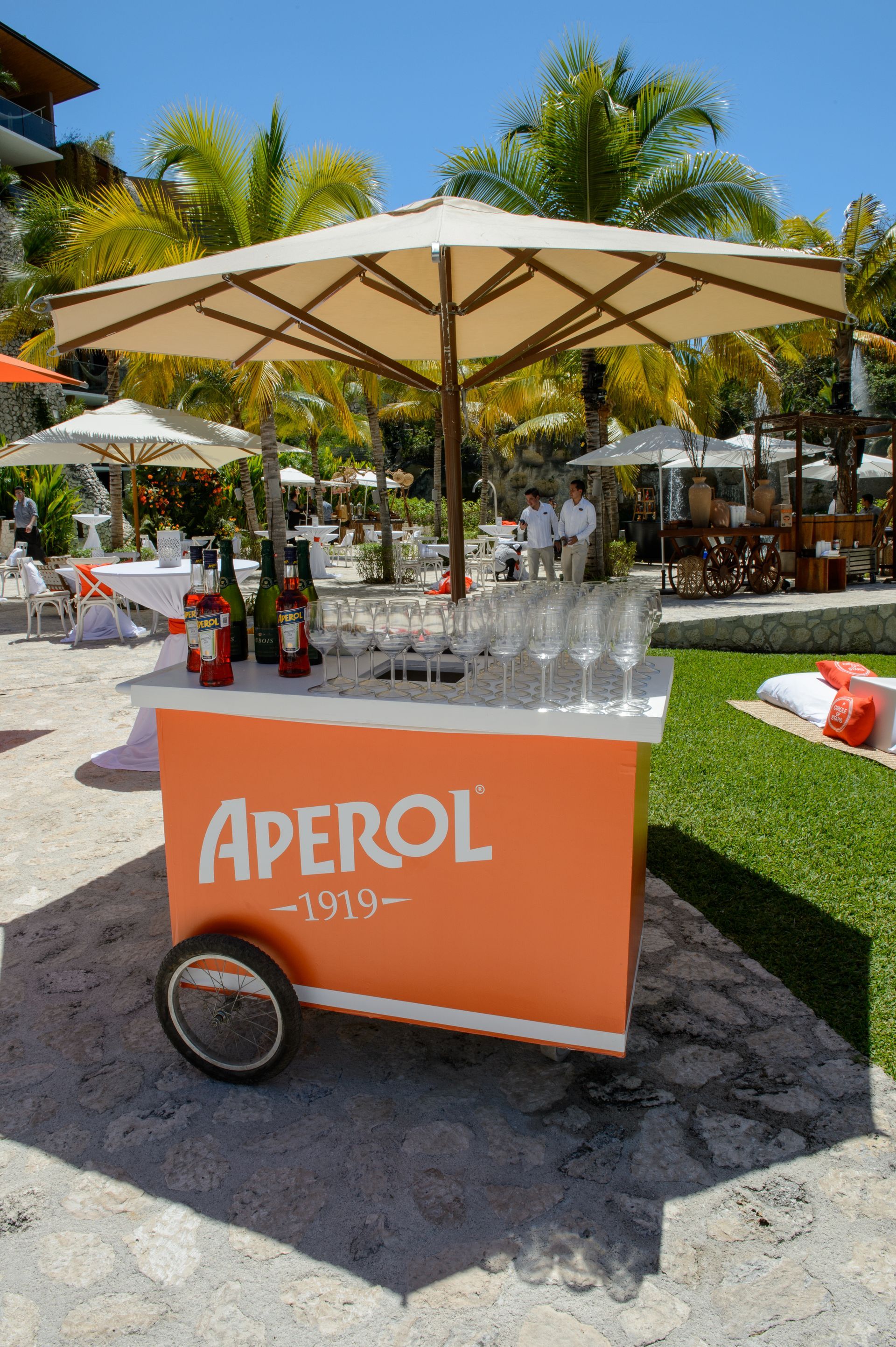 A cart with an umbrella and glasses of aperol on it