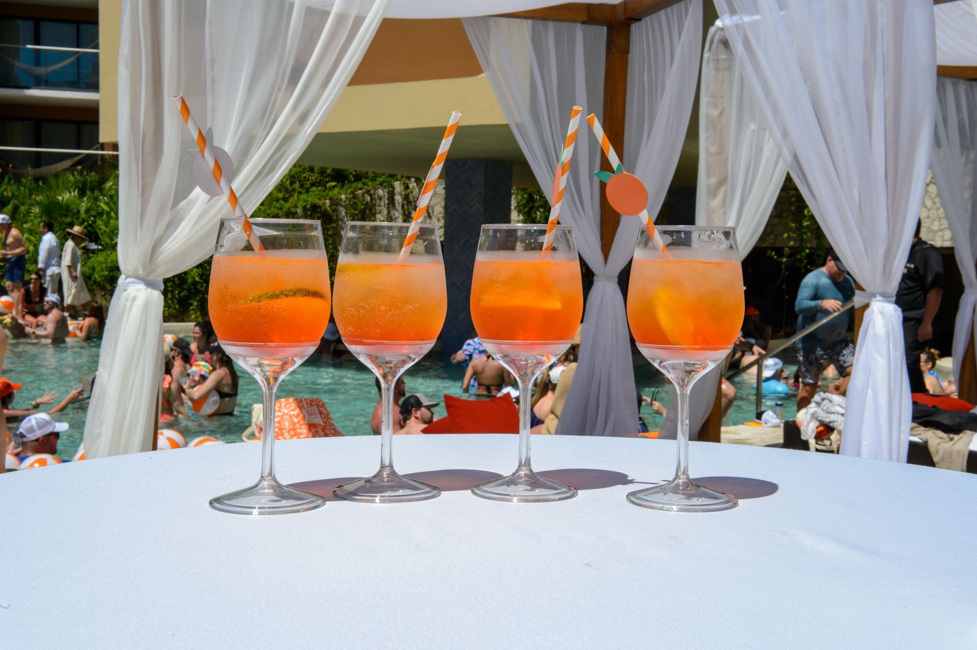 Three glasses of orange drinks with straws on a table in front of a pool.