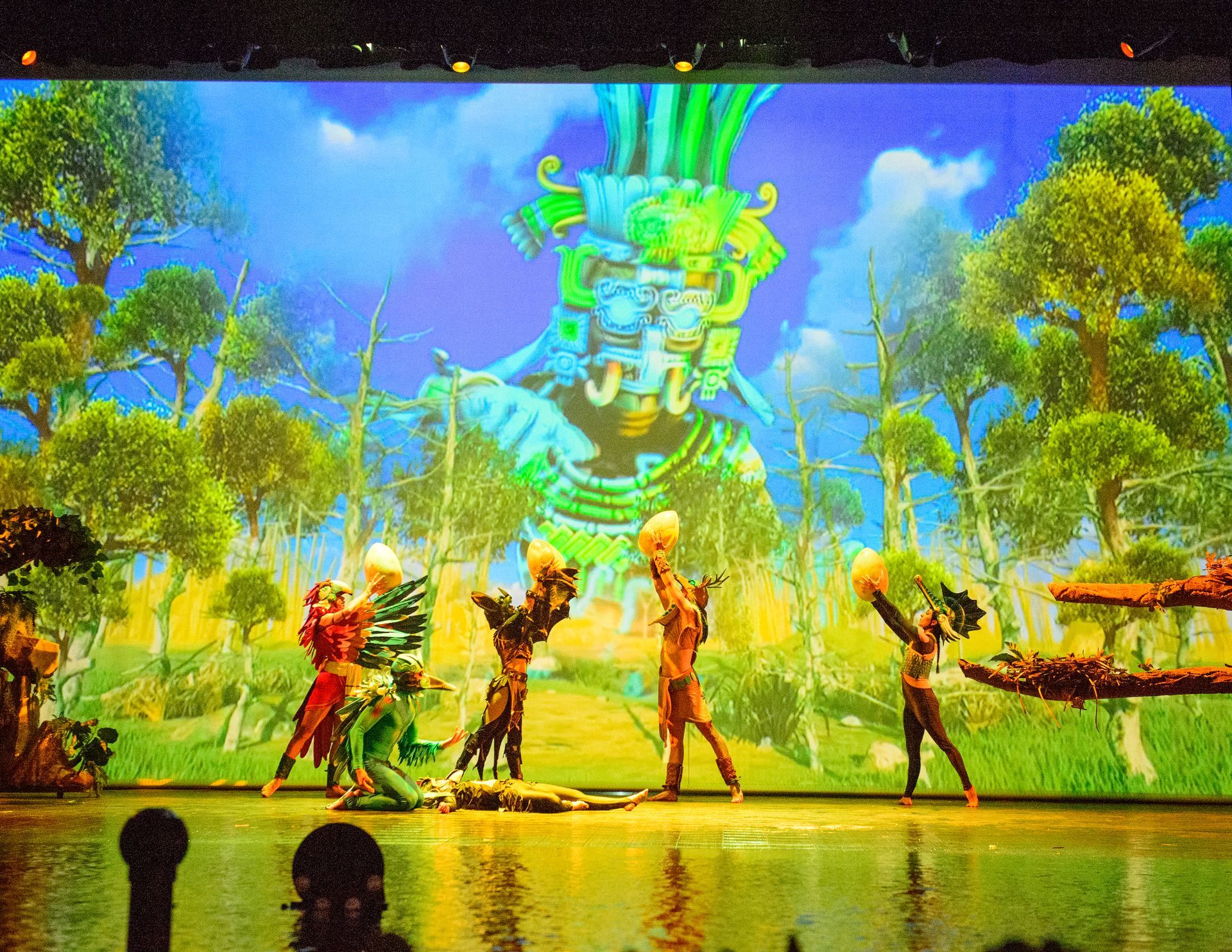 A group of people are dancing on a stage in front of a large screen.