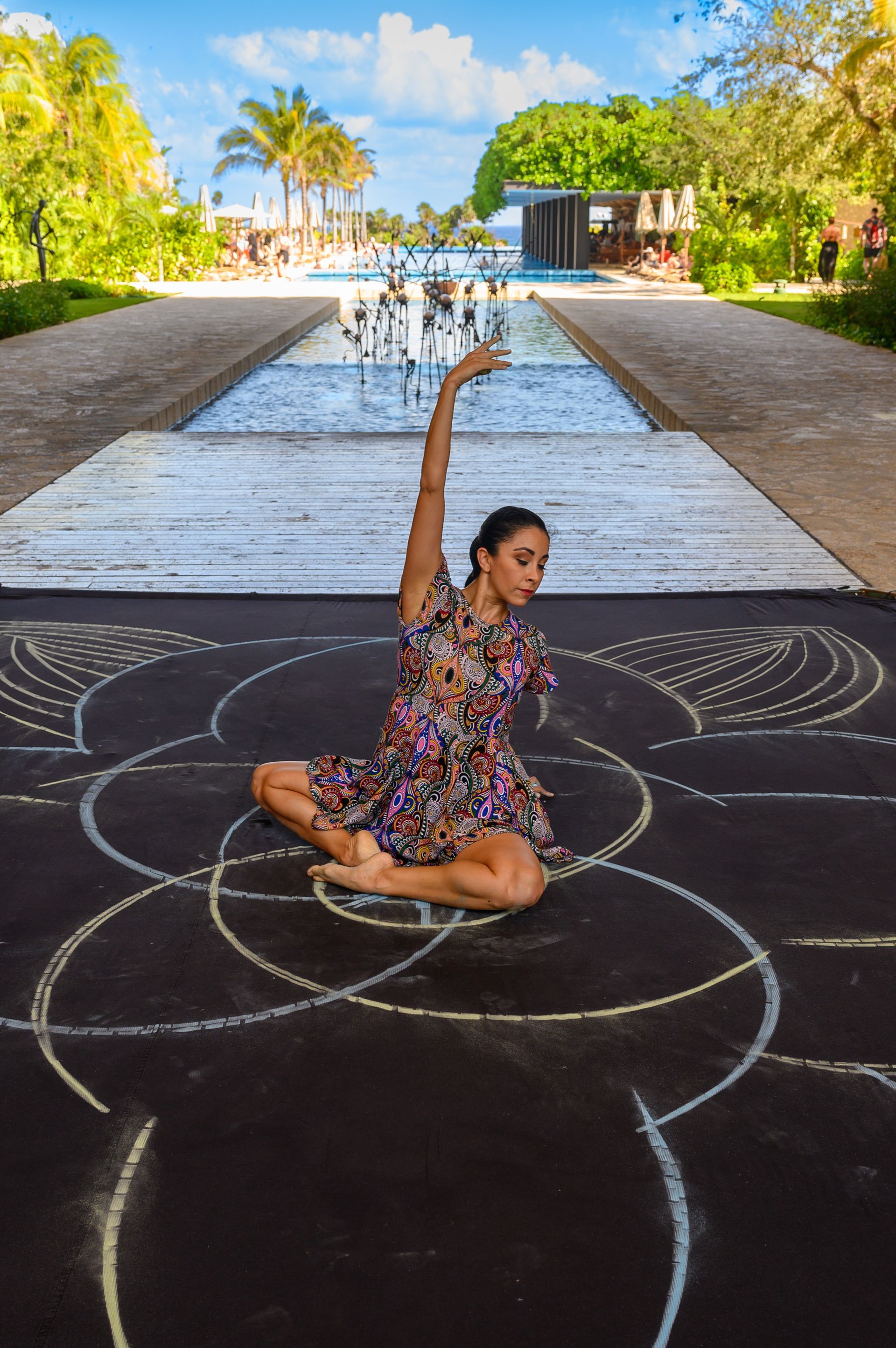 A woman in a dress is sitting on the ground in front of a fountain.