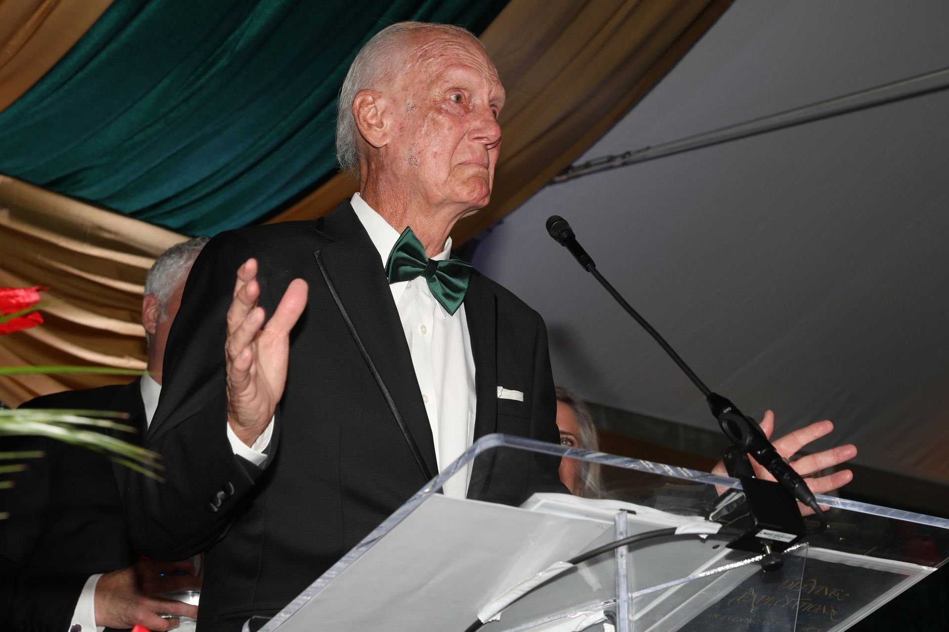 Man in tuxedo with green bow tie speaking at a podium.
