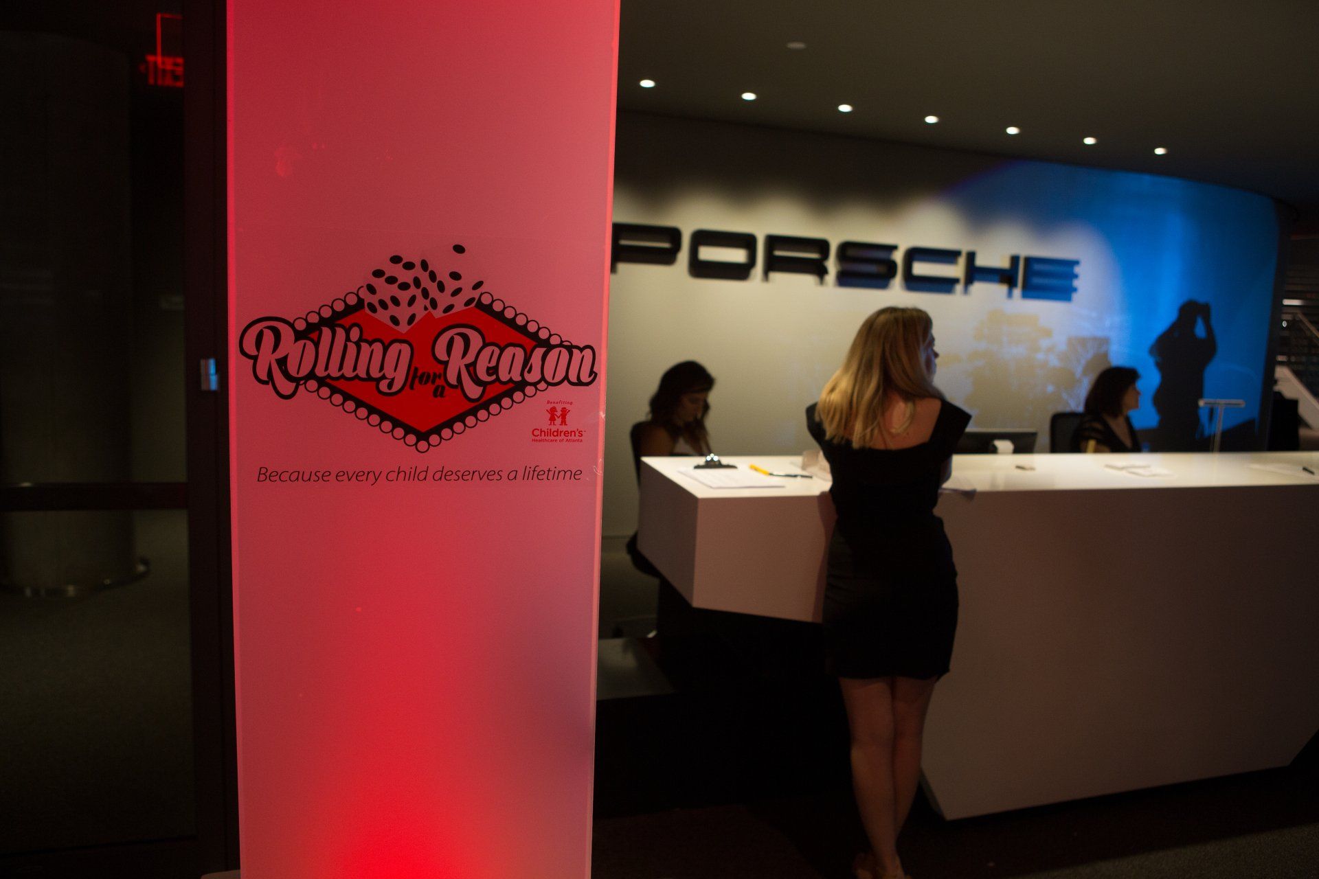 A woman is standing in front of a porsche sign