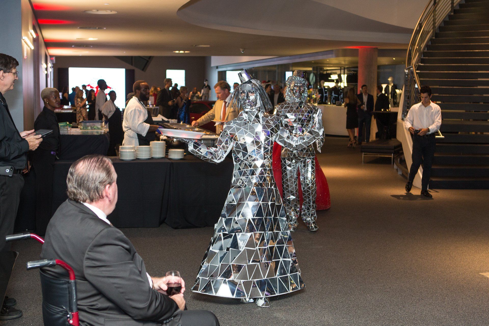 A man in a wheelchair is sitting in front of two mirrored robots