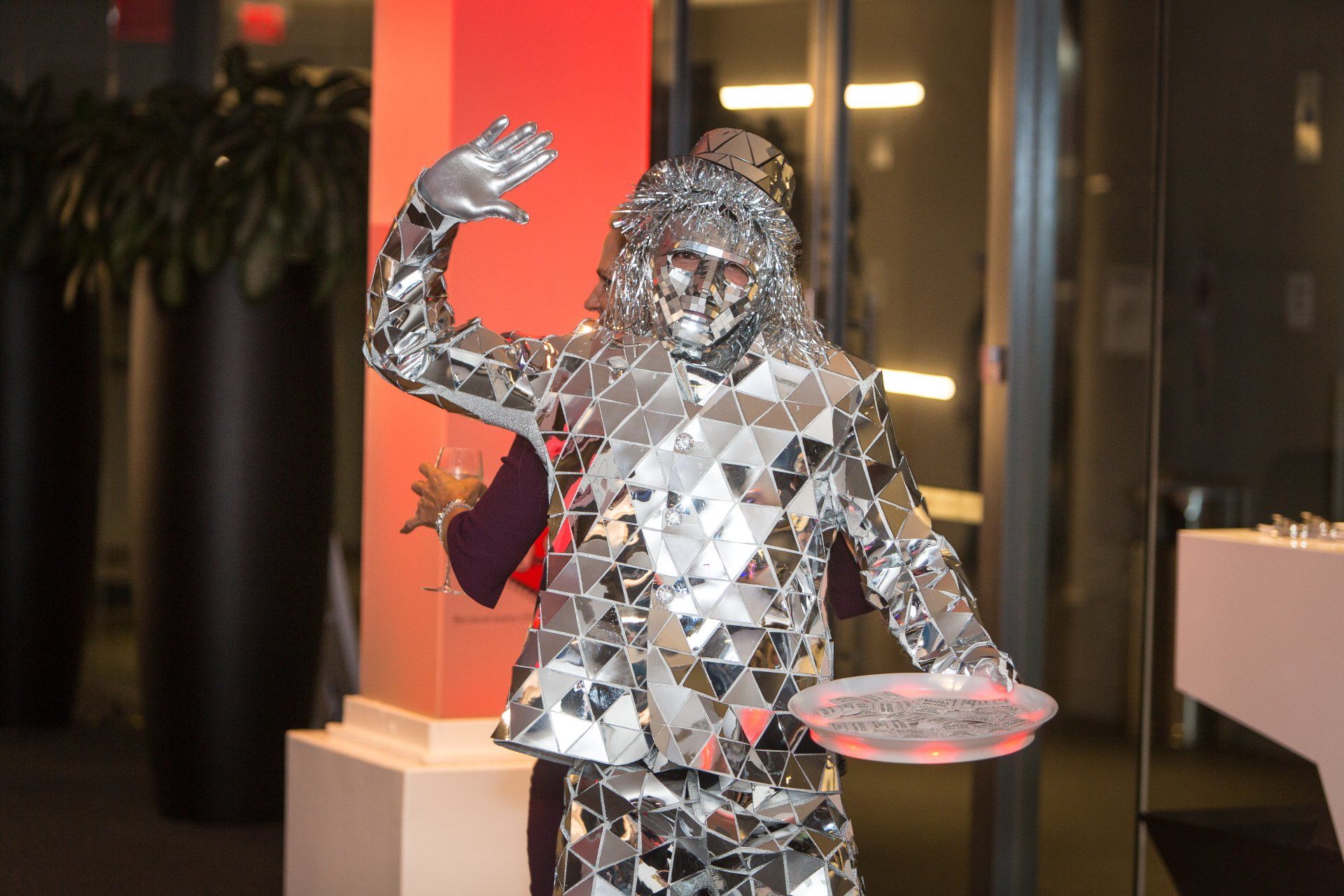 A man in a mirrored suit is holding a tray.