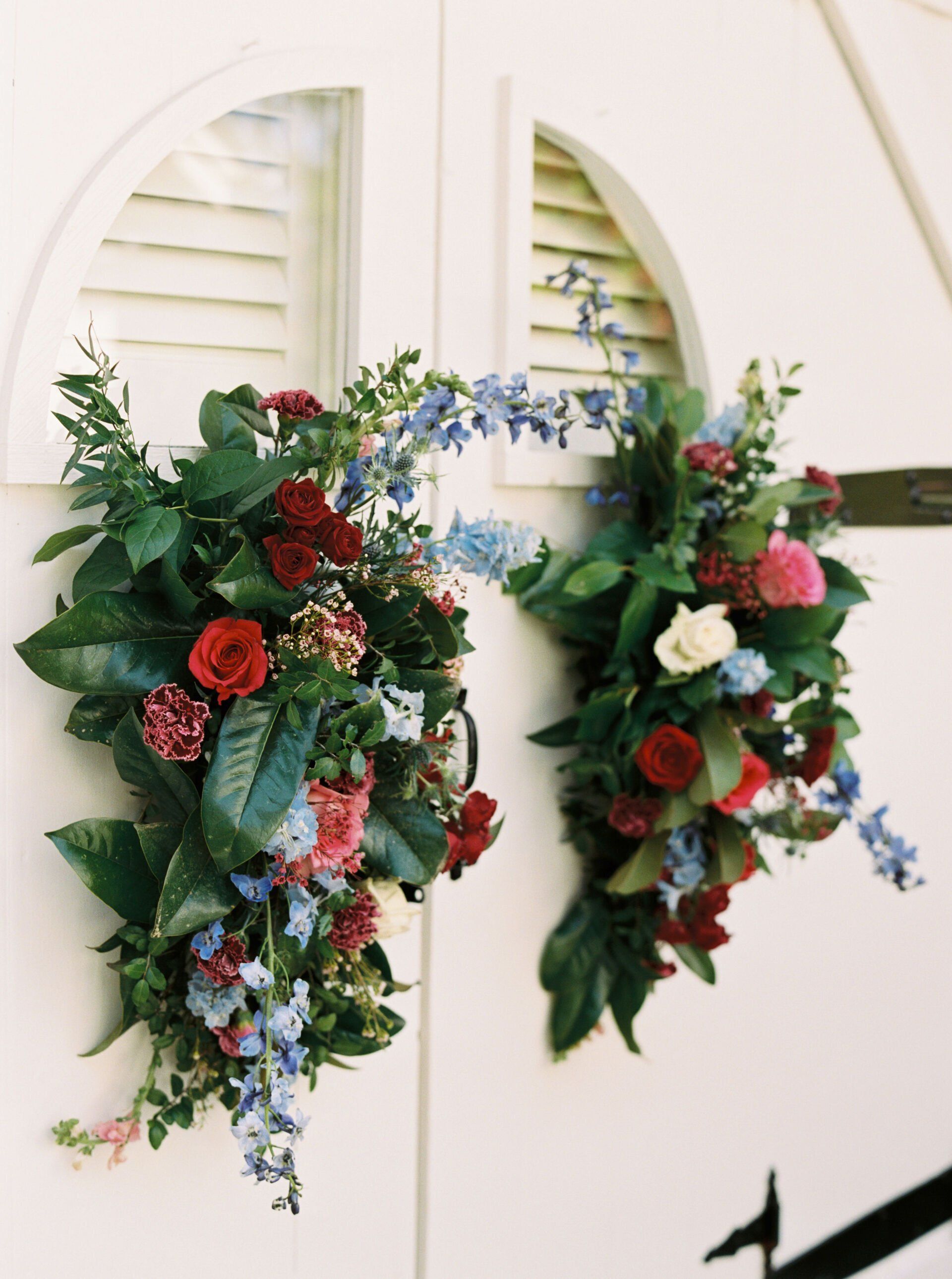 Two wreaths of flowers are hanging on a white door