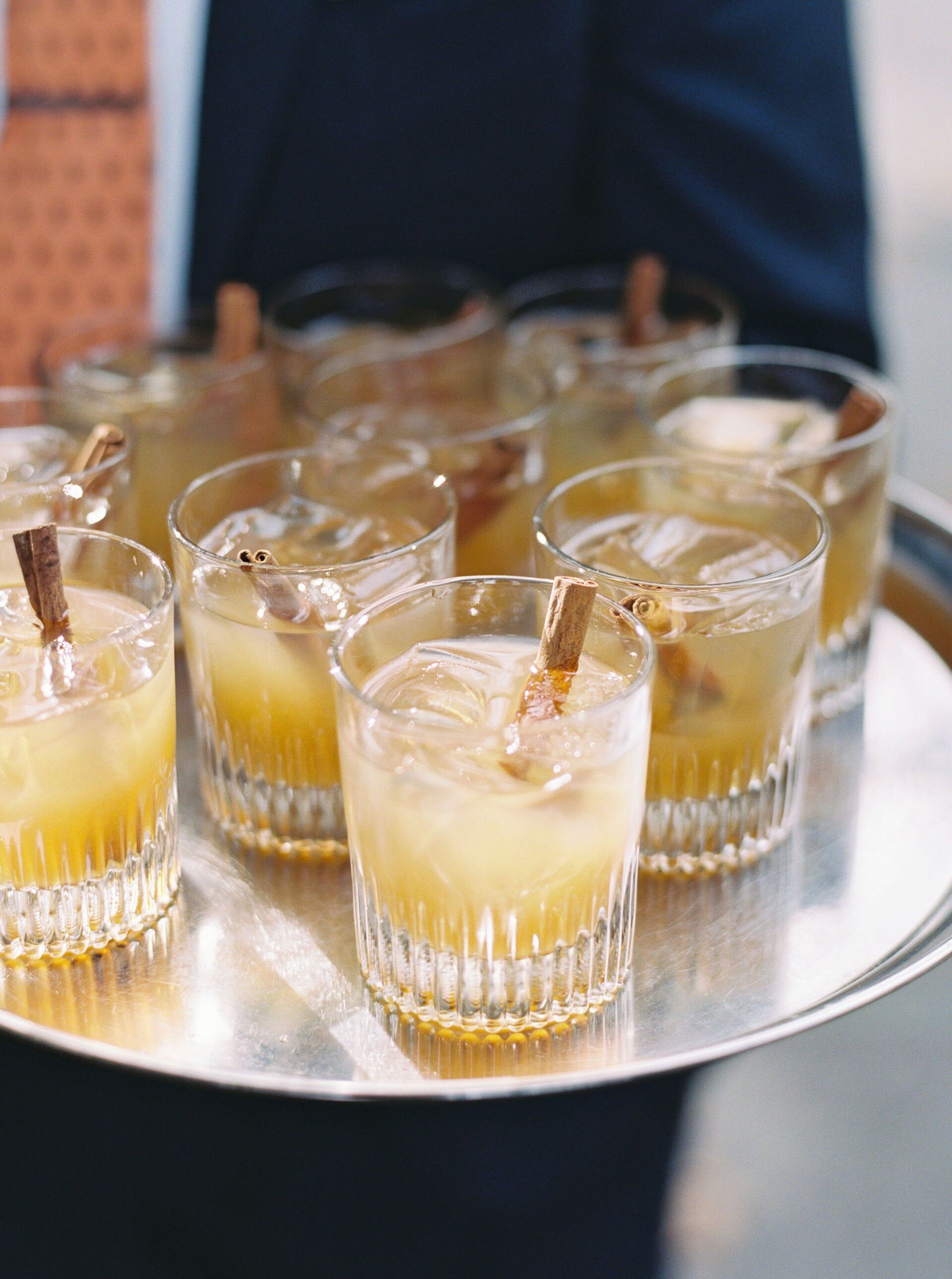 A person is holding a tray of drinks with cinnamon sticks in them